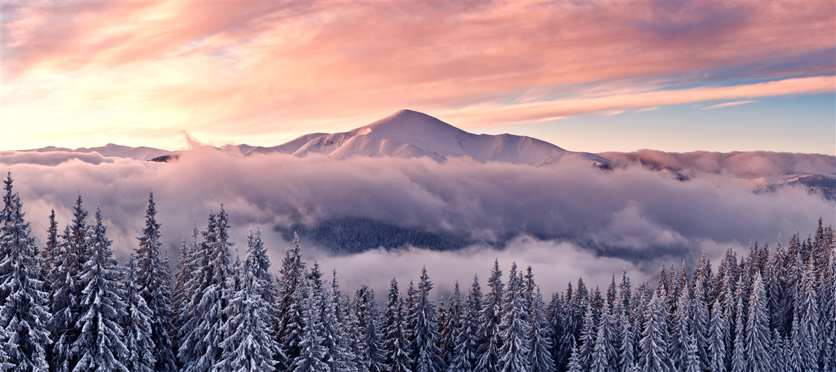 Papier peint Le coucher de soleil enveloppé de brume dans les montagnes peint l'espace dans des tons roses et froids.